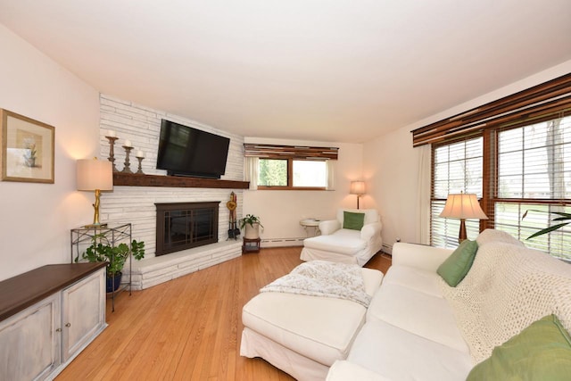 living room with light wood finished floors, a stone fireplace, and a baseboard radiator