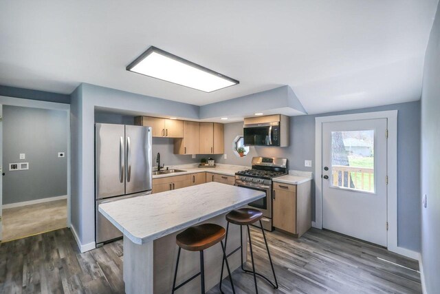 kitchen featuring wood finished floors, a kitchen bar, light countertops, a sink, and appliances with stainless steel finishes