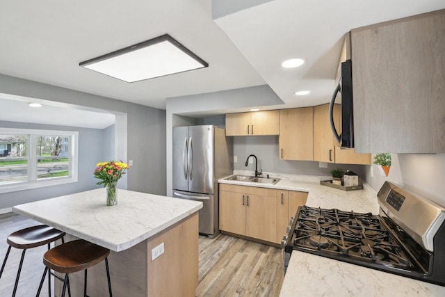 kitchen featuring light brown cabinets, a breakfast bar area, a center island, a sink, and appliances with stainless steel finishes