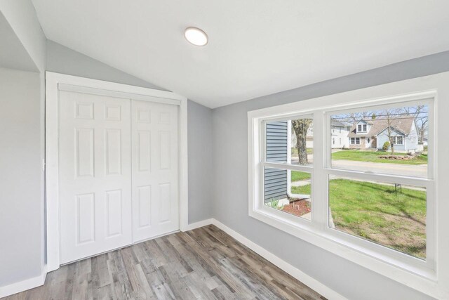 unfurnished bedroom with baseboards, vaulted ceiling, multiple windows, and wood finished floors
