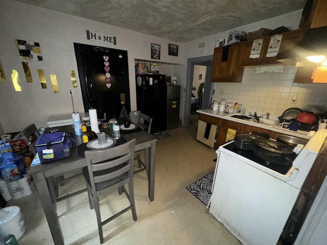 kitchen with decorative backsplash, light countertops, freestanding refrigerator, electric range, and light floors