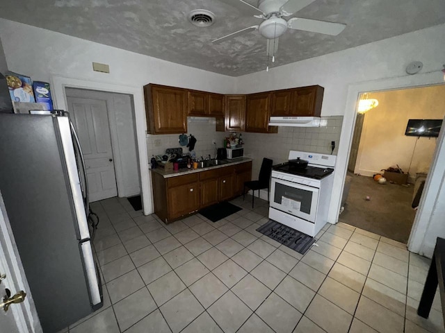 kitchen featuring freestanding refrigerator, under cabinet range hood, backsplash, white range with gas cooktop, and light tile patterned flooring