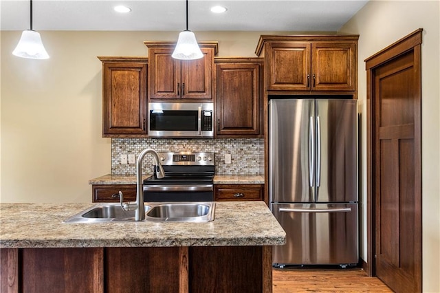 kitchen with stainless steel appliances, a sink, hanging light fixtures, light countertops, and decorative backsplash