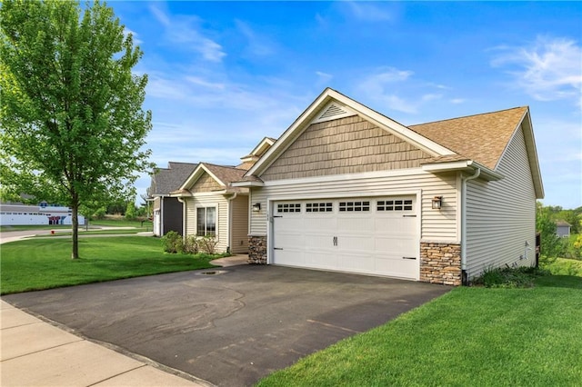 craftsman-style house with an attached garage, asphalt driveway, stone siding, a front yard, and roof with shingles