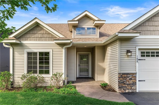 view of exterior entry with roof with shingles and a garage