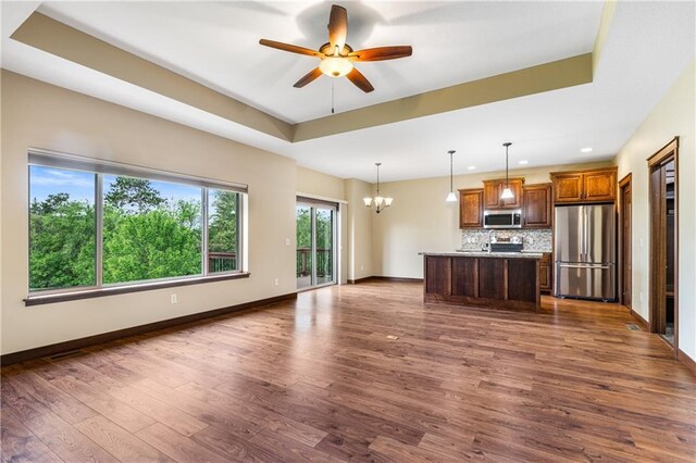 unfurnished living room featuring a chandelier, a raised ceiling, dark wood-style flooring, baseboards, and recessed lighting
