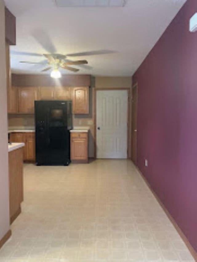 kitchen with brown cabinetry, a ceiling fan, light countertops, freestanding refrigerator, and light floors