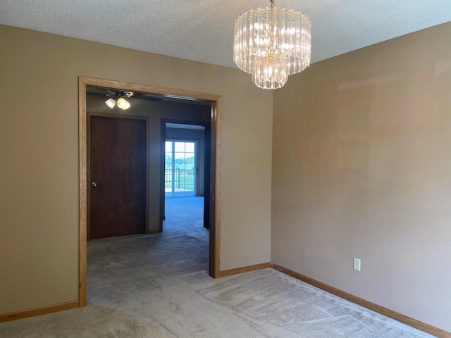empty room with a textured ceiling, a notable chandelier, light carpet, and baseboards