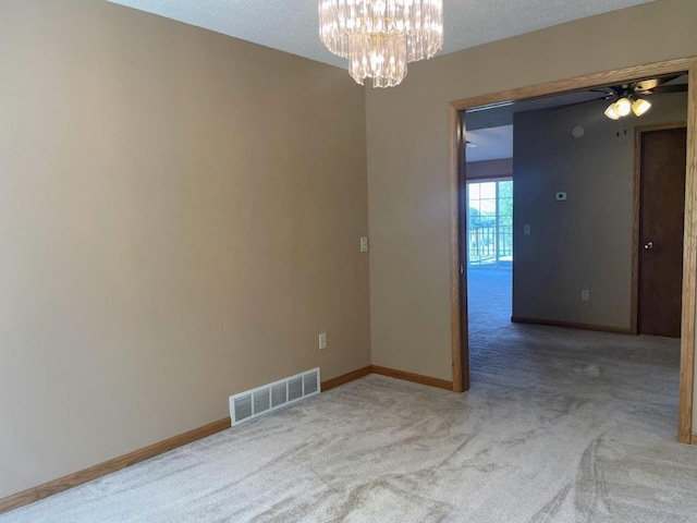spare room featuring ceiling fan with notable chandelier, visible vents, light carpet, and baseboards