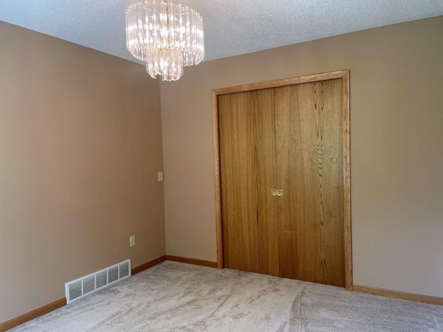 unfurnished bedroom with a chandelier, a closet, visible vents, carpet, and baseboards