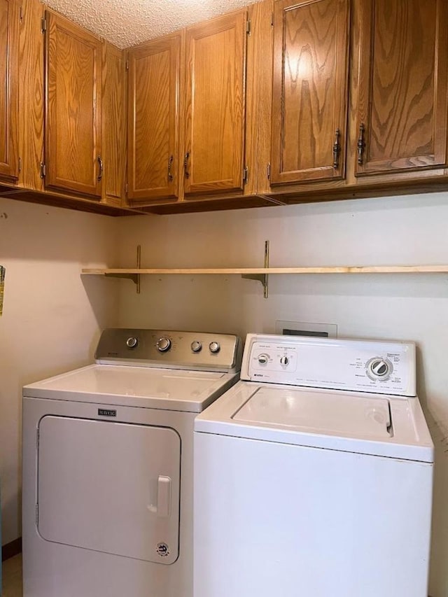 laundry room with a textured ceiling, washer and clothes dryer, and cabinet space