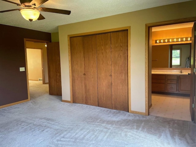 unfurnished bedroom with ceiling fan, a closet, baseboards, light carpet, and ensuite bath