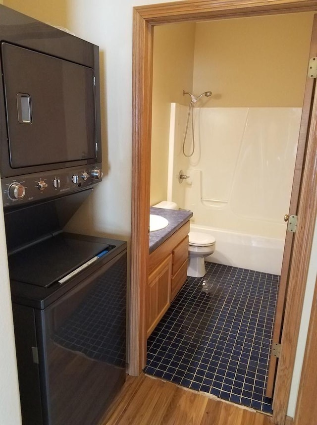 bathroom with stacked washer and clothes dryer, toilet, shower / bath combination, wood finished floors, and vanity