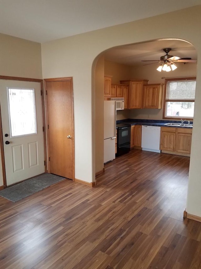 kitchen with a sink, white appliances, dark countertops, arched walkways, and dark wood finished floors