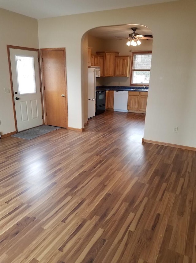 unfurnished living room with arched walkways, wood finished floors, a sink, baseboards, and a ceiling fan