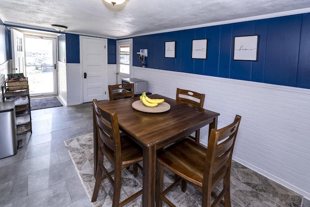 dining room with a wainscoted wall, a textured ceiling, and brick wall