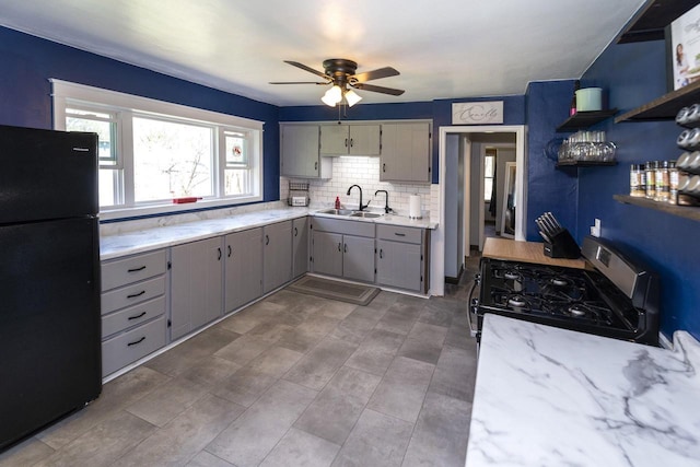 kitchen featuring stainless steel gas range, a sink, gray cabinets, a ceiling fan, and freestanding refrigerator
