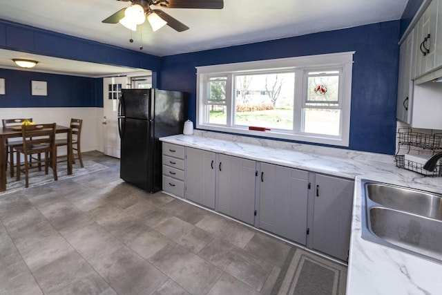 kitchen with a sink, gray cabinetry, ceiling fan, and freestanding refrigerator