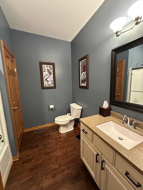 full bathroom with walk in shower, wood finished floors, vanity, baseboards, and toilet