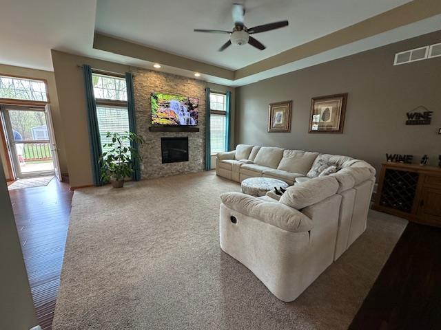 living area featuring a raised ceiling, visible vents, a ceiling fan, and a wealth of natural light