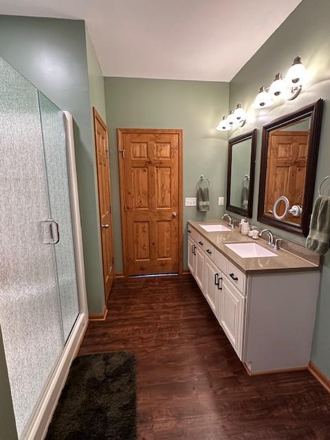 full bath featuring double vanity, a stall shower, a sink, and wood finished floors