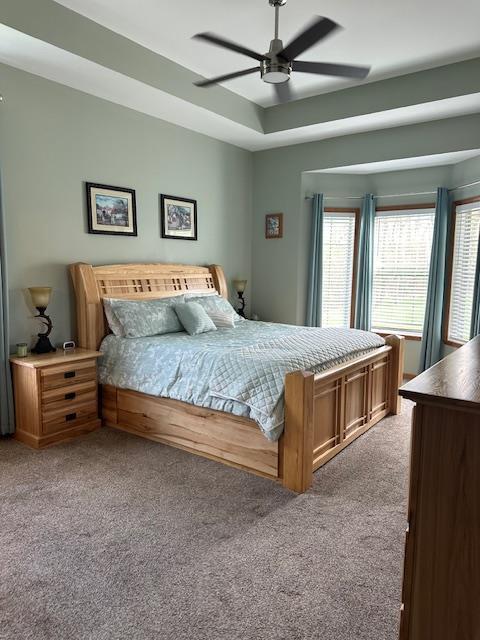 carpeted bedroom with a ceiling fan and a tray ceiling