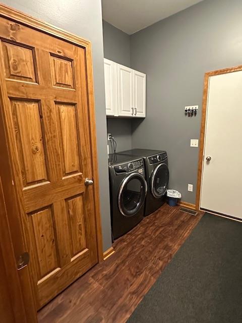 washroom featuring cabinet space, baseboards, dark wood finished floors, and washer and clothes dryer