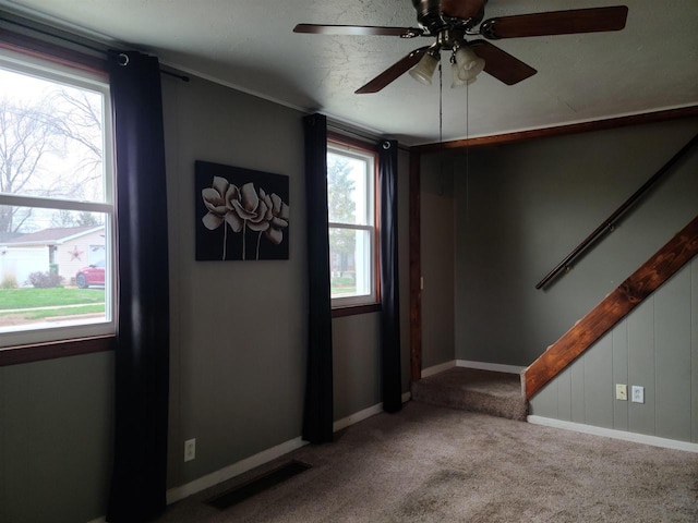 empty room with stairway, visible vents, baseboards, carpet, and a ceiling fan