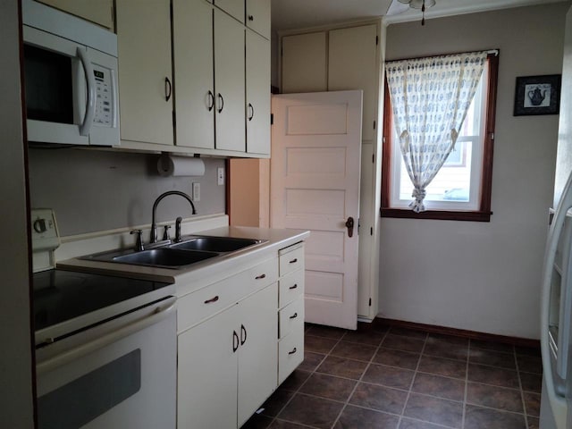 kitchen with white appliances, dark tile patterned flooring, white cabinetry, a sink, and baseboards