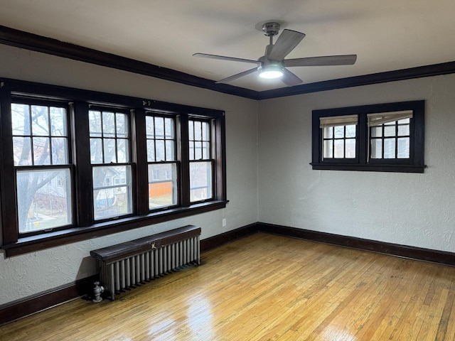 empty room featuring a ceiling fan, radiator heating unit, light wood-style flooring, and baseboards
