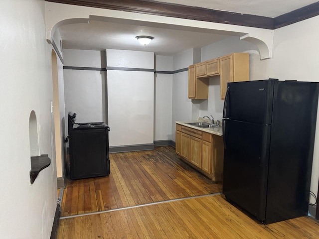 kitchen featuring arched walkways, freestanding refrigerator, hardwood / wood-style flooring, light countertops, and a sink