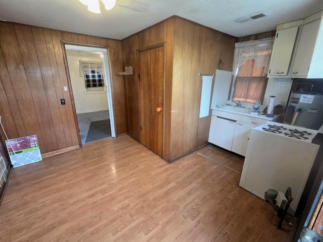 kitchen with visible vents, wood walls, a sink, light countertops, and light wood-style flooring