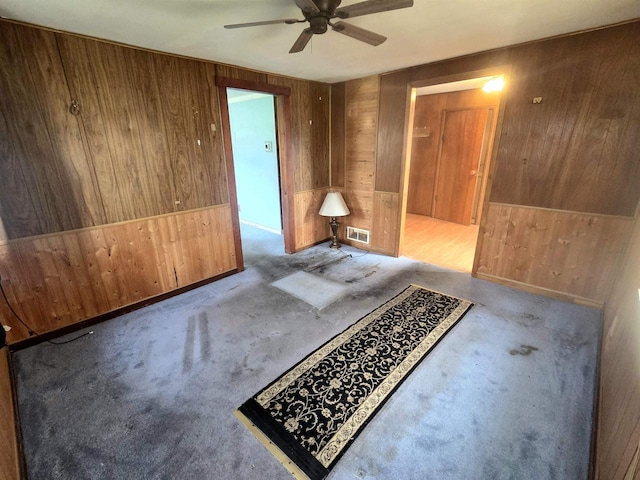 interior space featuring wooden walls, ceiling fan, carpet, and visible vents