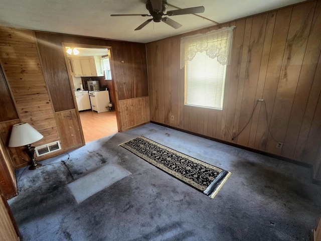 unfurnished living room with wooden walls, ceiling fan, visible vents, and carpet floors