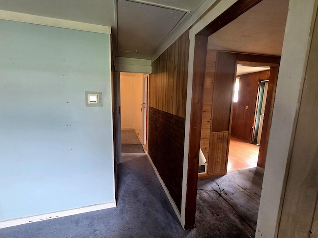 hall with wooden walls, carpet floors, and attic access