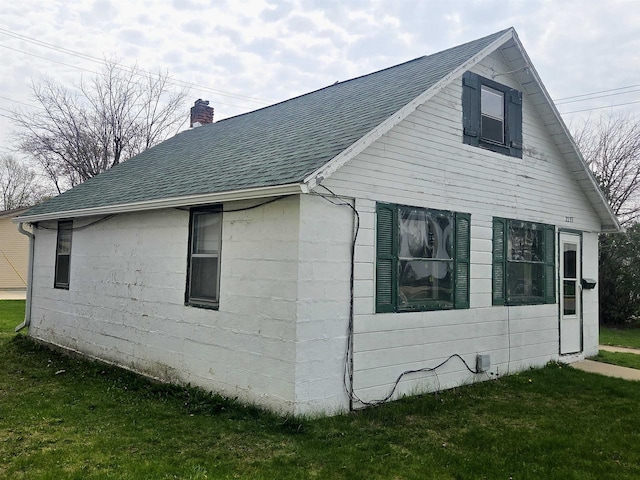 view of side of home featuring a yard, a shingled roof, and a chimney