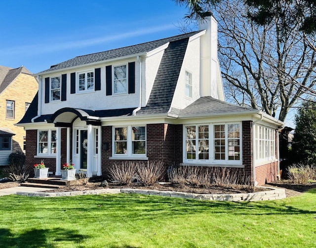 dutch colonial with a chimney, a front yard, roof with shingles, and brick siding