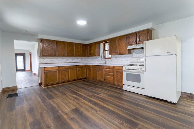 kitchen with white appliances, under cabinet range hood, light countertops, backsplash, and dark wood-style floors