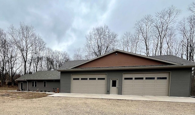 exterior space featuring driveway, roof with shingles, and a detached garage
