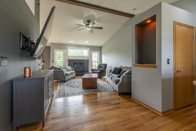living area featuring ceiling fan, a brick fireplace, baseboards, vaulted ceiling with beams, and wood finished floors