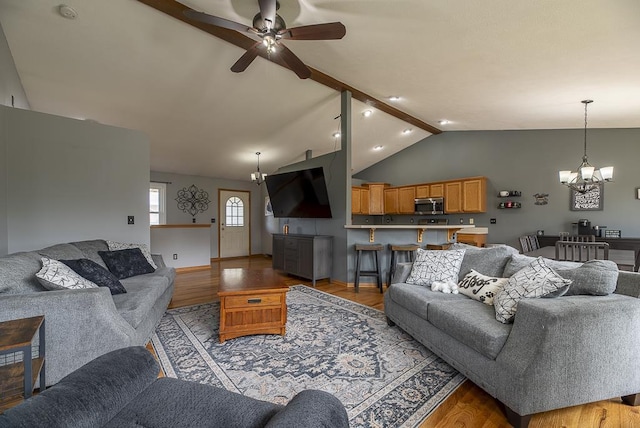 living room featuring lofted ceiling with beams, light wood-style flooring, and ceiling fan with notable chandelier