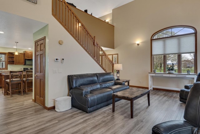 living area with light wood finished floors, a high ceiling, stairway, and baseboards