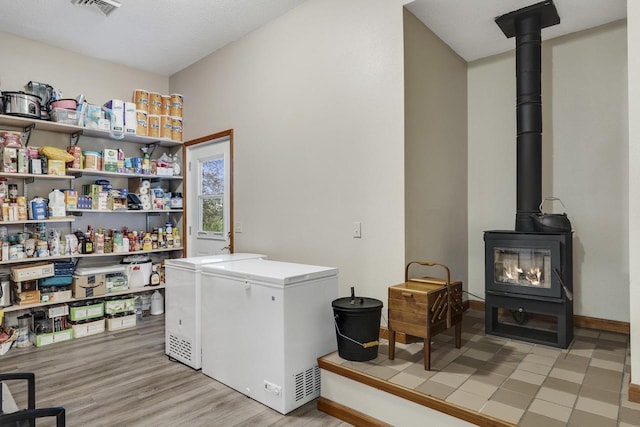 laundry area with a wood stove, light wood-style floors, separate washer and dryer, visible vents, and baseboards