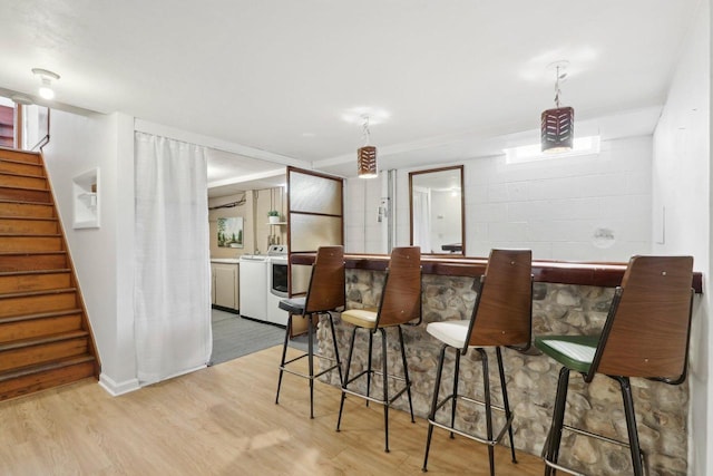 bar featuring a dry bar, concrete block wall, washer / clothes dryer, stairs, and wood finished floors