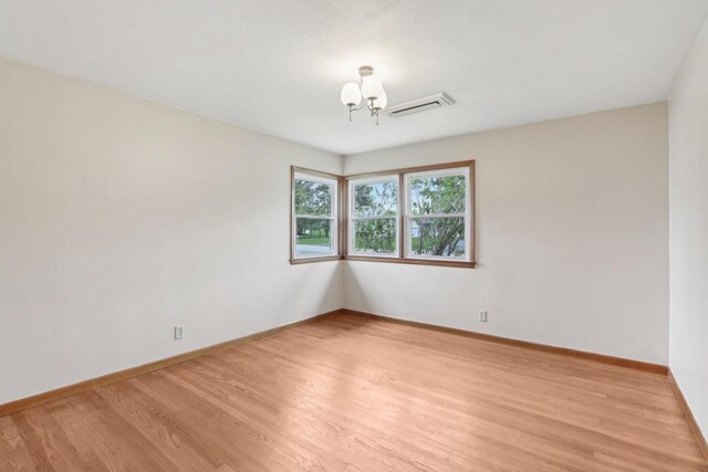 unfurnished room with baseboards, visible vents, light wood finished floors, and a chandelier