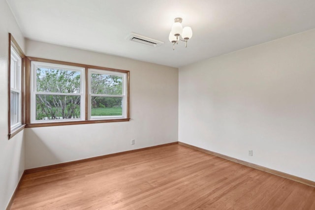 empty room with baseboards, a chandelier, visible vents, and light wood-style floors