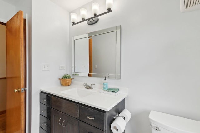 half bathroom with vanity, toilet, and visible vents