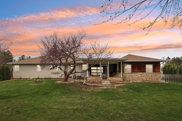 back of house at dusk featuring a lawn, fence, and stone siding