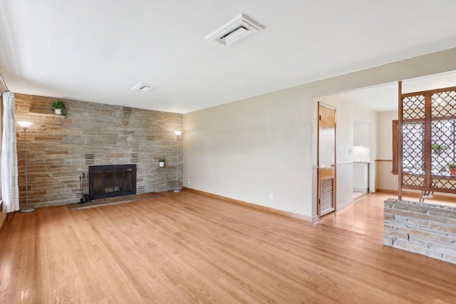 unfurnished living room with a stone fireplace, light wood finished floors, baseboards, and visible vents