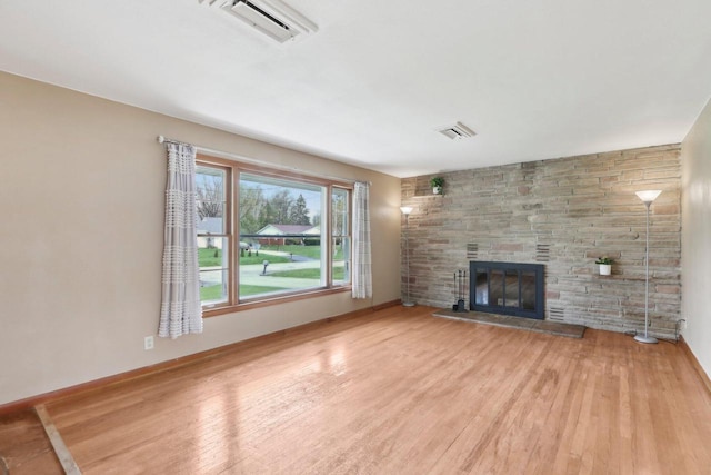 unfurnished living room featuring visible vents, a stone fireplace, and light wood-type flooring